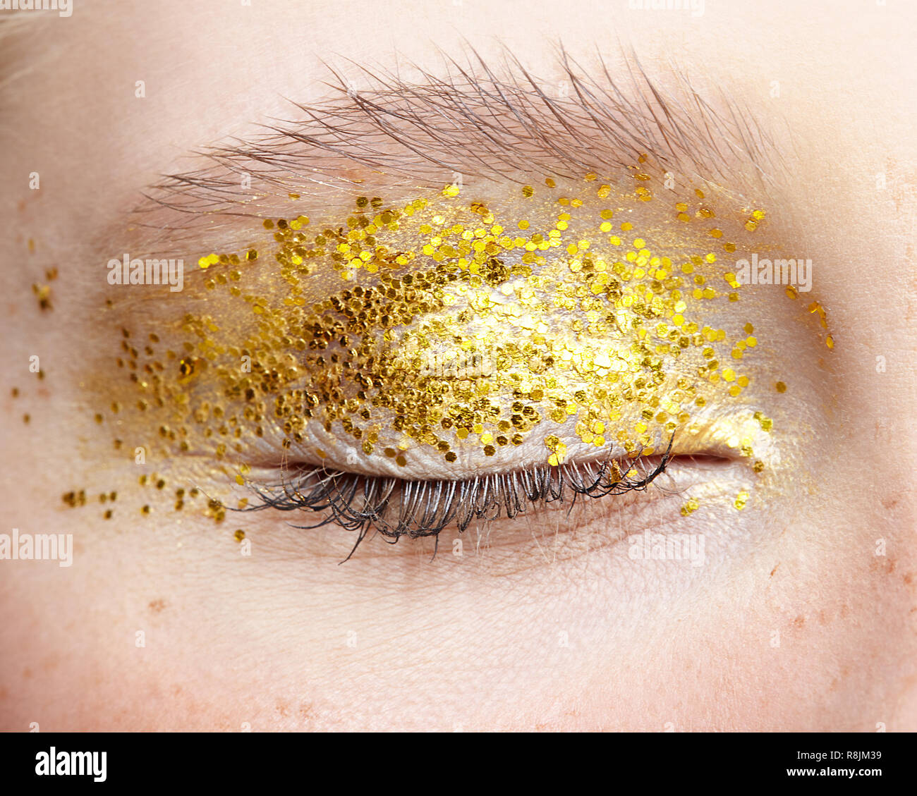 Macro Closeup colpo di umano chiuso occhio femmina. Donna con insoliti glitter scintillante vogue bellezza viso trucco. Ragazza con una pelle perfetta e giallo smoky ey Foto Stock