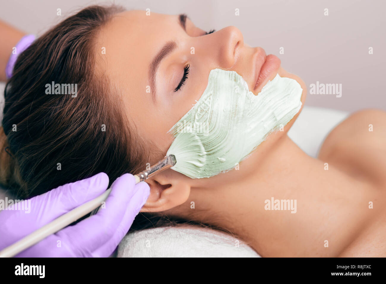 Terapista di bellezza applicare un peeling viso maschera per una donna faccia per il ringiovanimento cutaneo Foto Stock