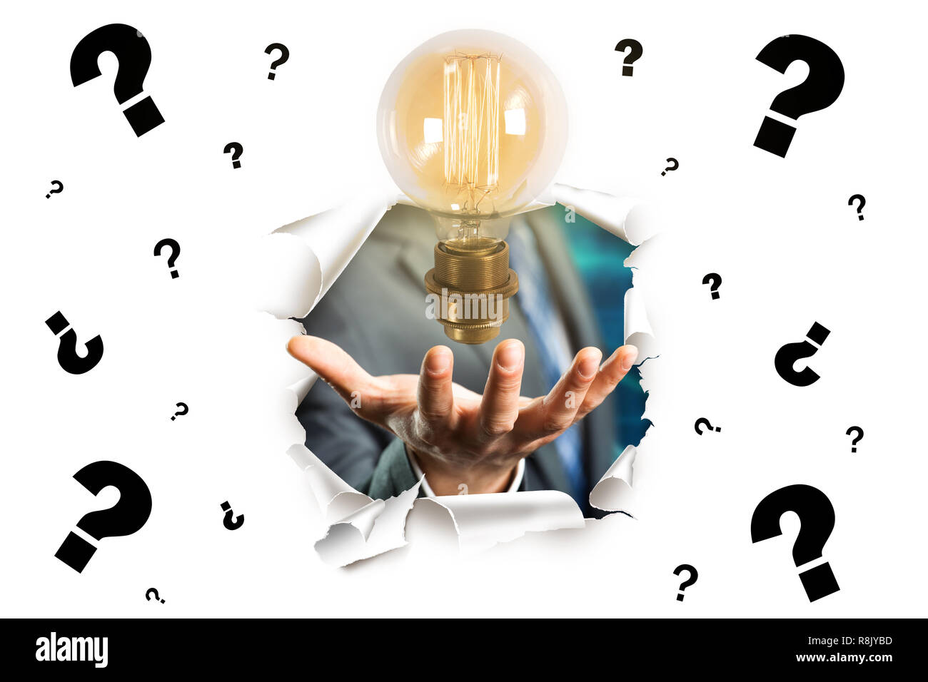 Imprenditore presentando una lampadina elettrica come la migliore idea rottura attraverso una parete di carta con molti questionmarks su di esso Foto Stock