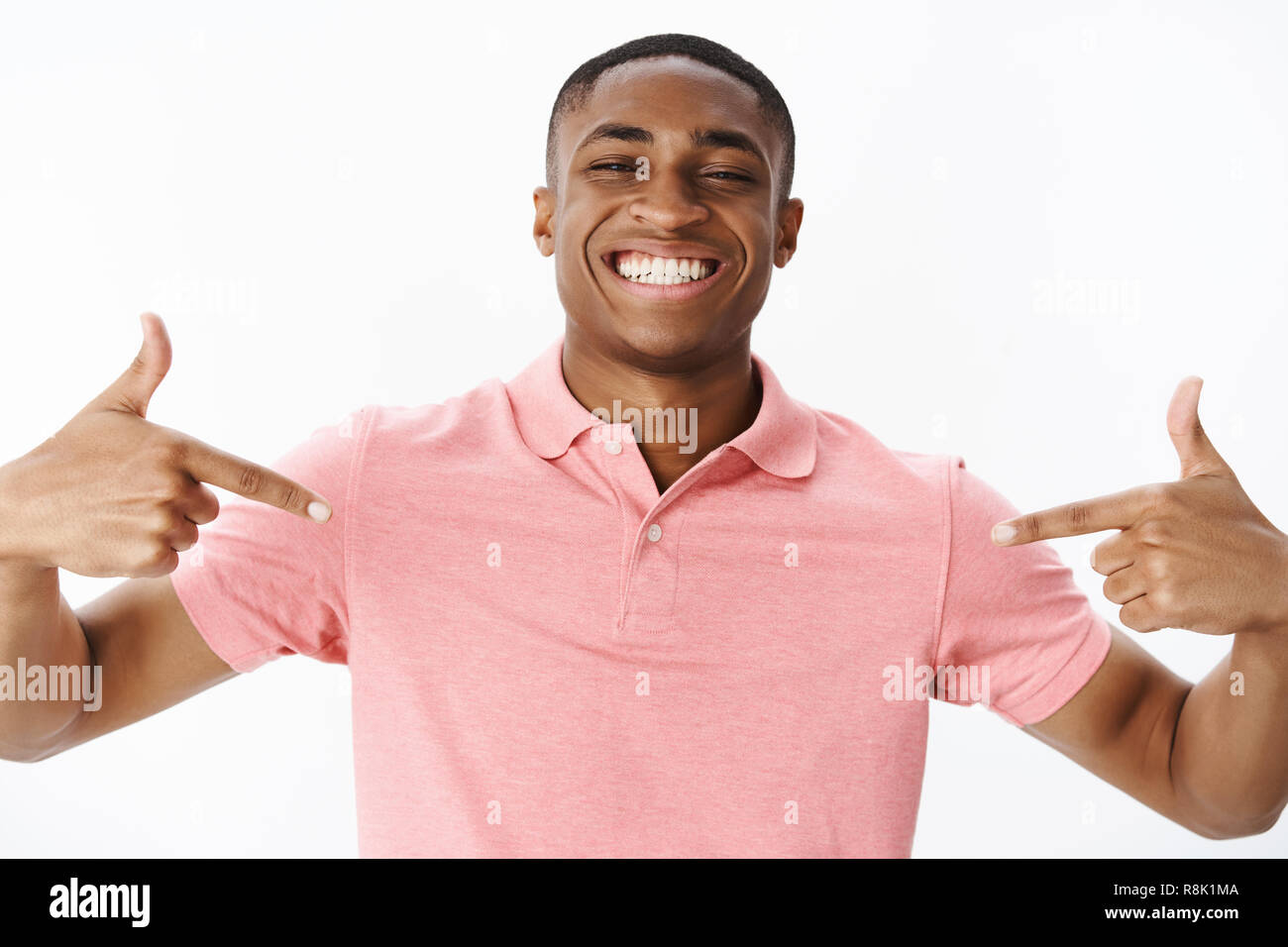 Vincitore fiero rivolto a se stesso sentimento di auto-soddisfatto e onorato la ricezione di aggiudicazione sorridente gioiosamente con bianco denti perfetta posa in rosa polo shirt fiducioso e soddisfatto su sfondo grigio Foto Stock