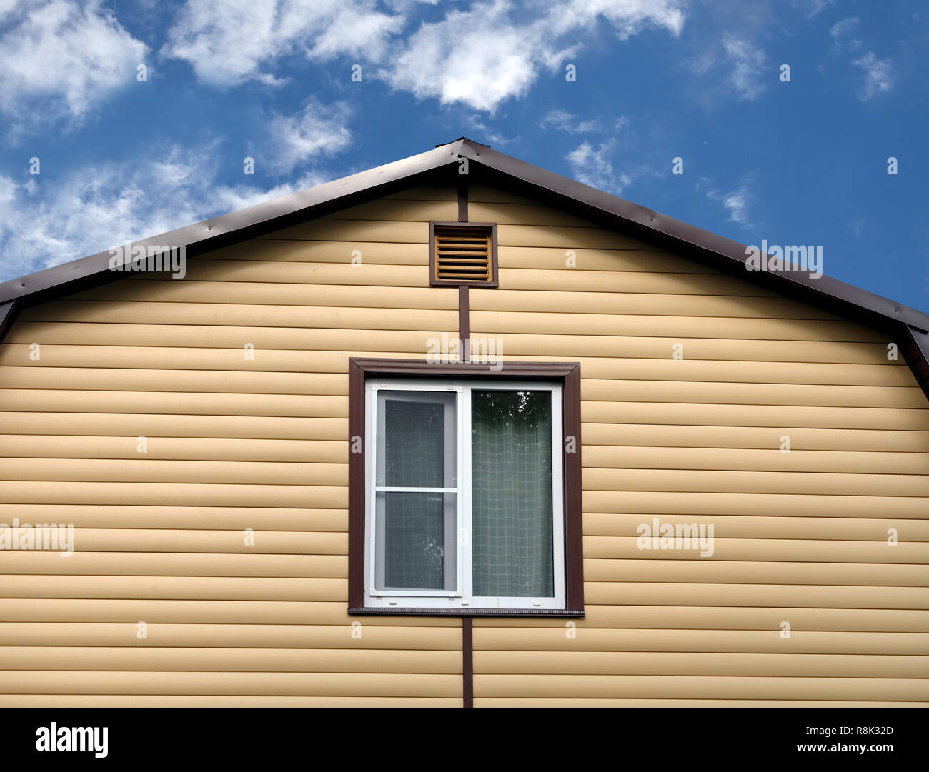 La sezione superiore della moderna casa di campagna privata parete ricoperta con schierandosi giallo e marrone e tetto metallico sul cielo blu con nuvole sulla giornata soleggiata vista frontale Foto Stock