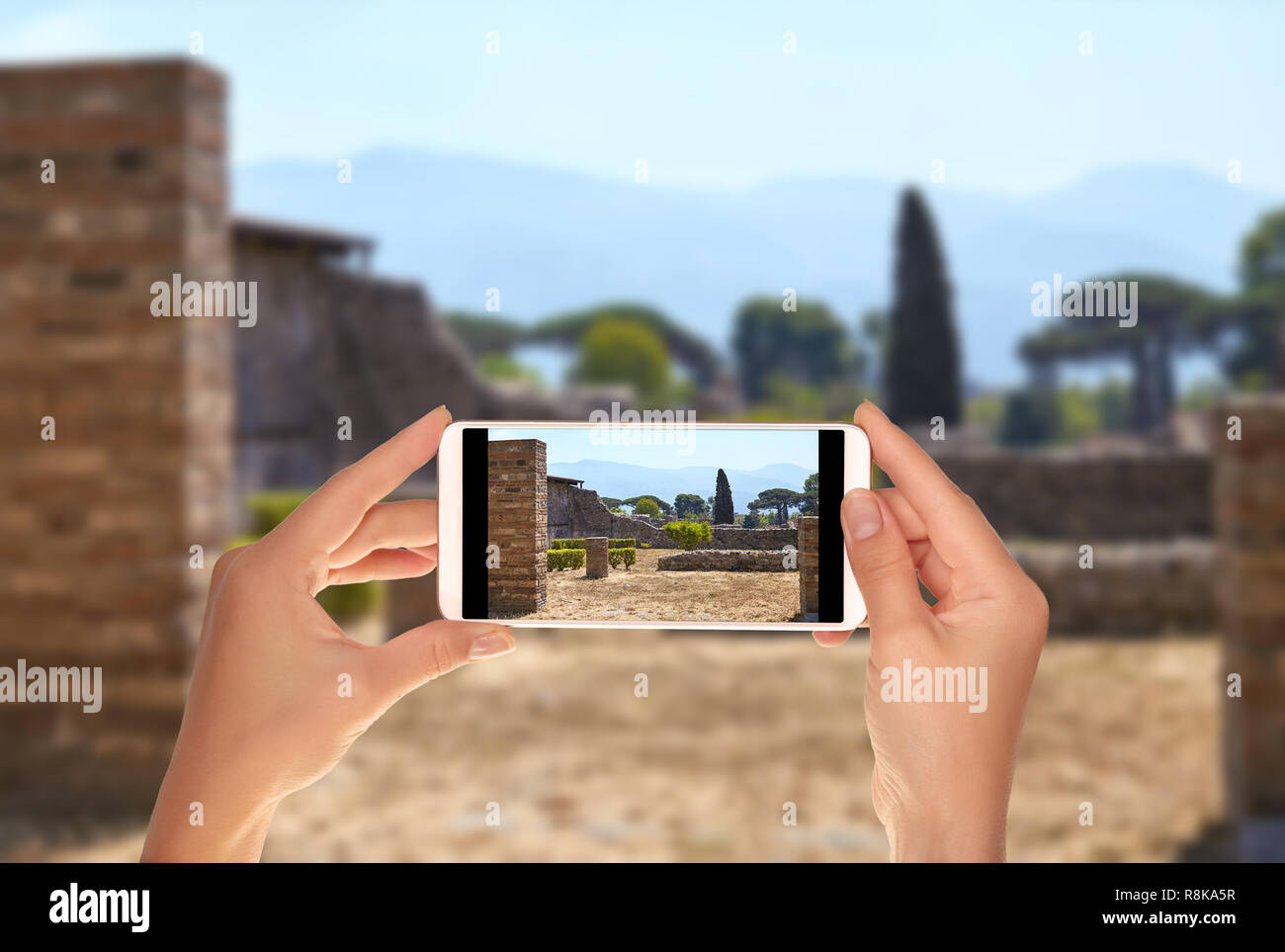 Un turista è di scattare una foto di una strada senza le persone con i resti di case di Pompei con il Vesuvio sullo sfondo a un telefono cellulare Foto Stock
