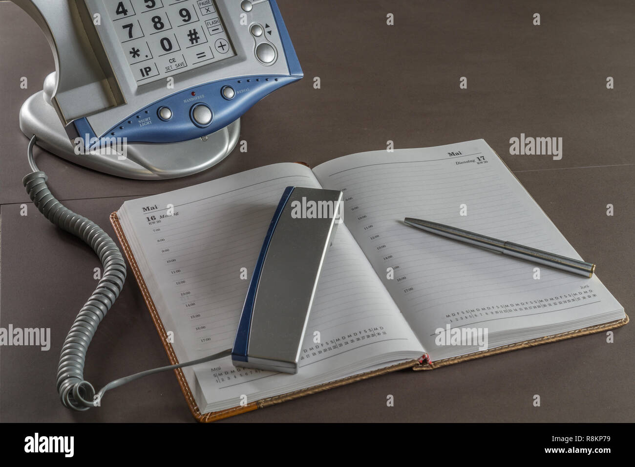 Un telefono su una scrivania in ufficio con una calandra libro. il calendario Foto Stock