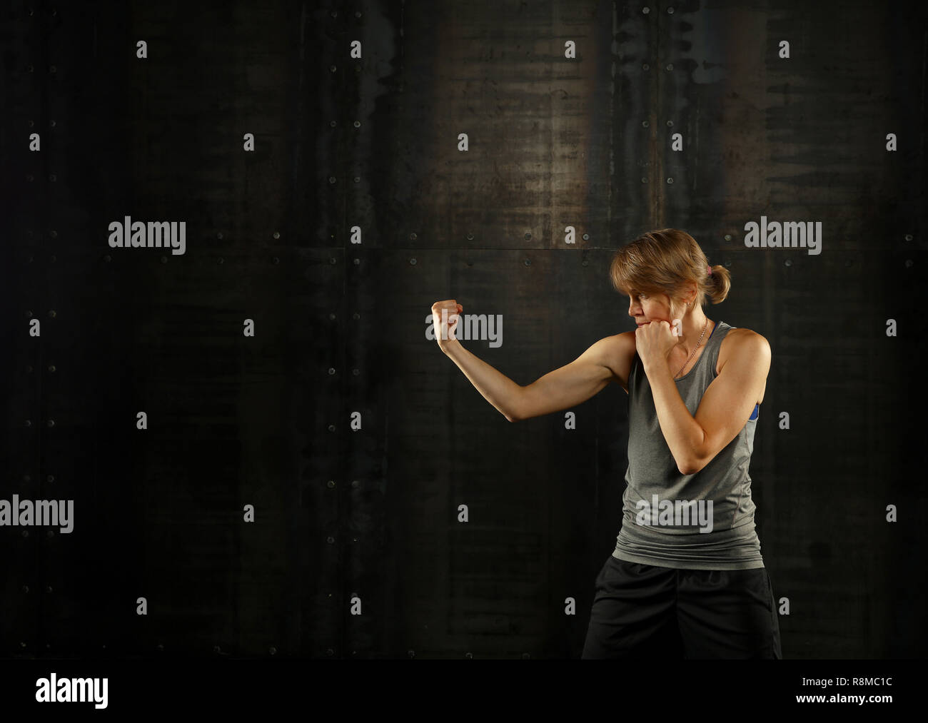 Close up side Visualizza profilo ritratto di una giovane età media athletic donna shadow boxing in abbigliamento sportivo in palestra su sfondo scuro, guardando lontano Foto Stock