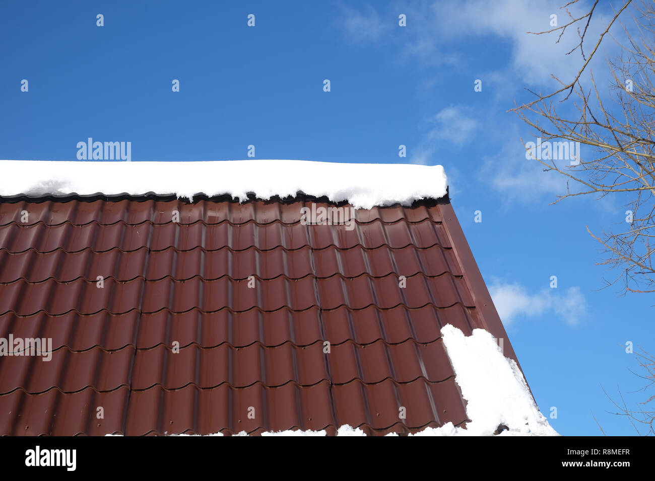 Lato del country house il tetto dalla brown Piastrella in metallo con cumulo di neve nella soleggiata giornata di primavera sotto il cielo blu con nuvole bianche vista laterale Foto Stock