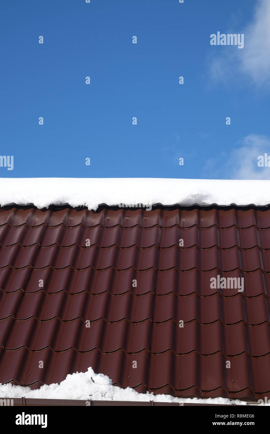Lato del country house il tetto dalla brown Piastrella in metallo con neve nella soleggiata giornata di primavera sotto il cielo blu con nuvole bianche vista frontale Foto Stock