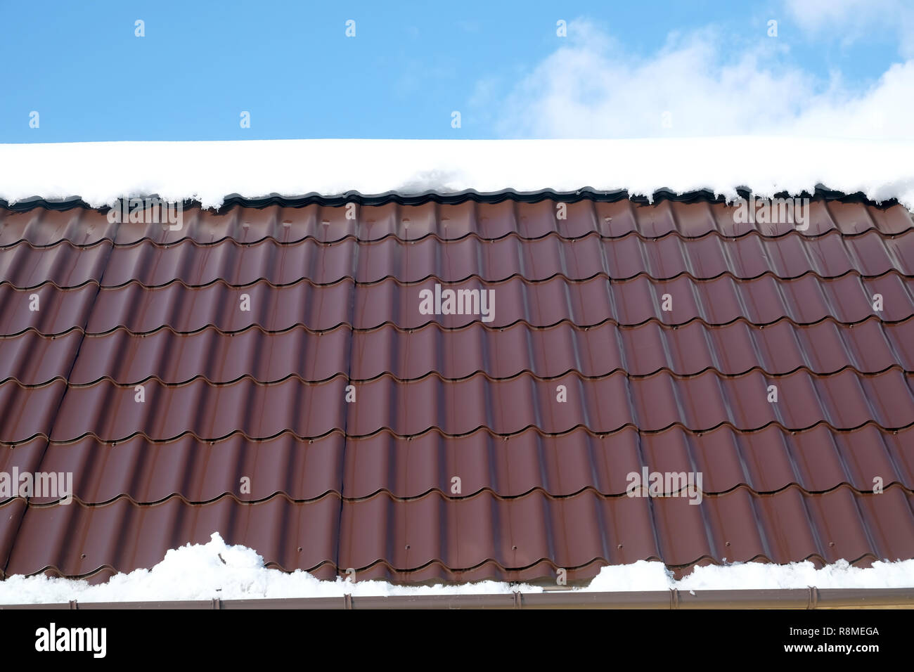 Lato del country house il tetto dalla brown Piastrella in metallo con neve nella soleggiata giornata di primavera sotto il cielo blu con nuvole bianche vista frontale Foto Stock