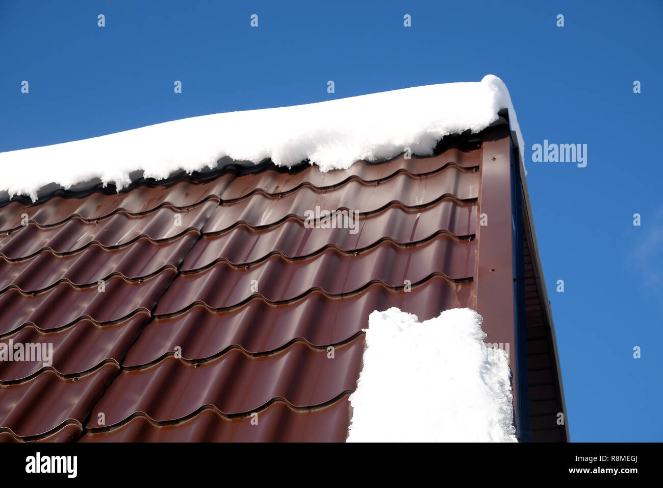 Lato del country house il tetto dalla brown Piastrella in metallo con cumulo di neve nella soleggiata giornata di primavera sotto il cielo blu con nuvole bianche vista laterale Foto Stock