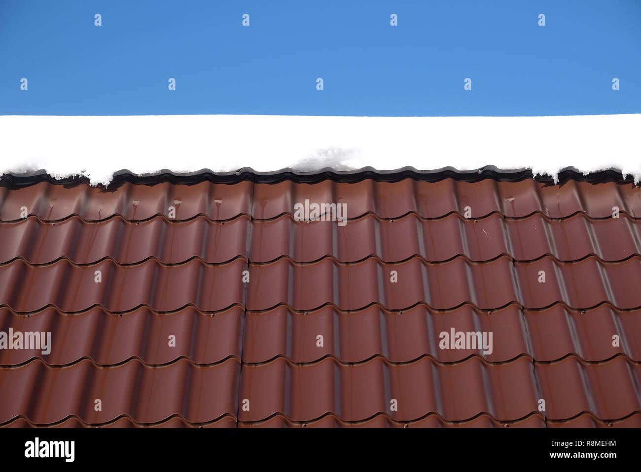 Lato del country house il tetto dalla brown Piastrella in metallo con neve nella soleggiata giornata di primavera sotto il cielo blu con nuvole bianche vista frontale Foto Stock