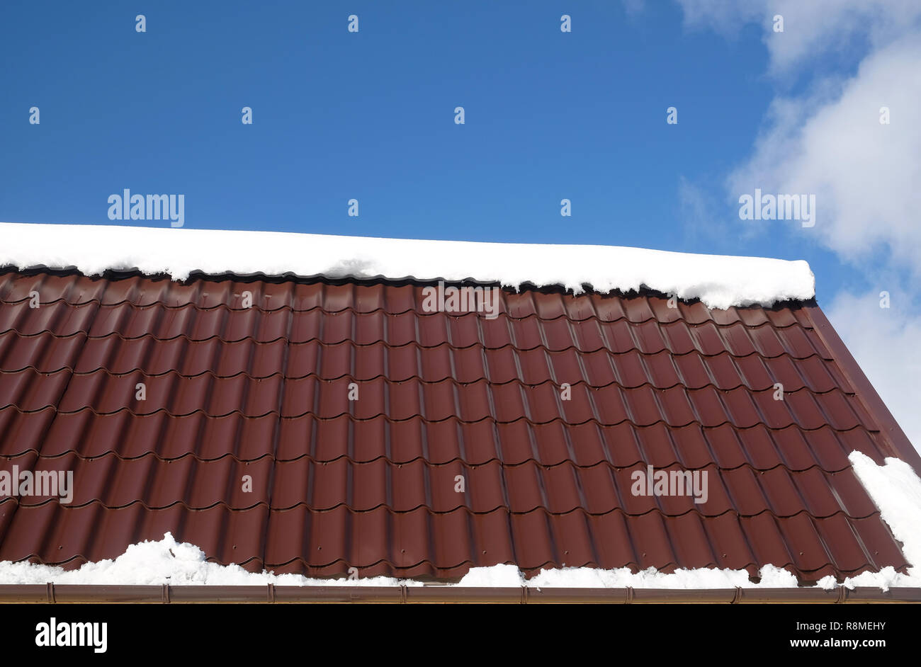 Lato del country house il tetto dalla brown Piastrella in metallo con cumulo di neve nella soleggiata giornata di primavera sotto il cielo blu con nuvole bianche vista laterale Foto Stock