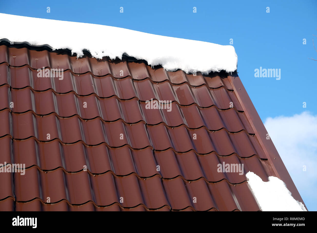 Lato del country house il tetto dalla brown Piastrella in metallo con cumulo di neve nella soleggiata giornata di primavera sotto il cielo blu con nuvole bianche vista laterale Foto Stock