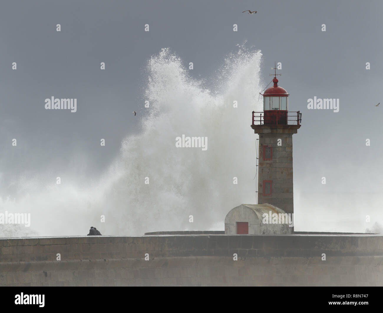 Un enorme mare tempestoso wave oltre il molo vecchio e del faro alla foce del fiume Douro vedendo audaci persone indistinto Foto Stock
