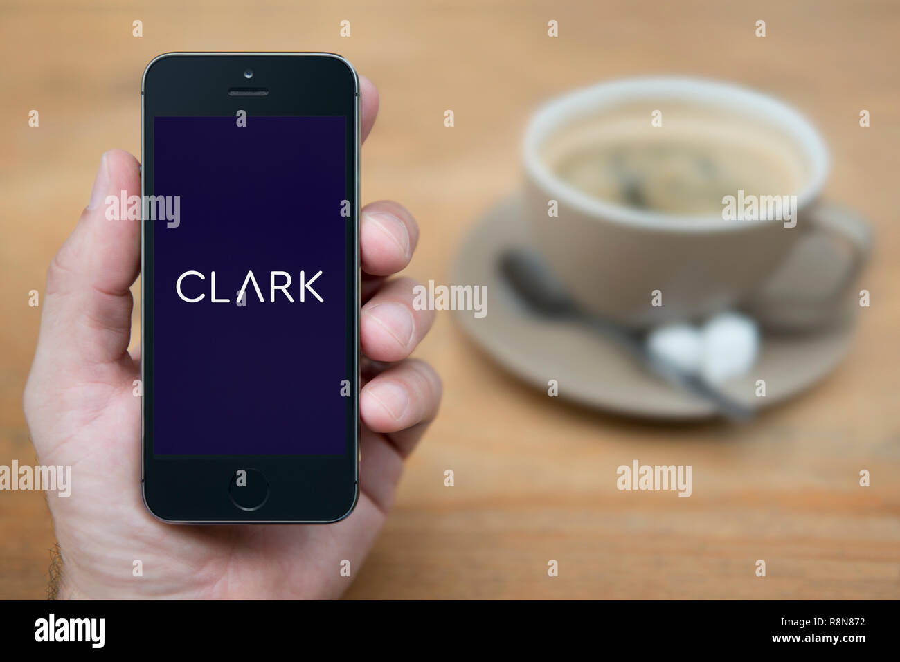 Un uomo guarda al suo iPhone che visualizza il logo di Clark (solo uso editoriale). Foto Stock