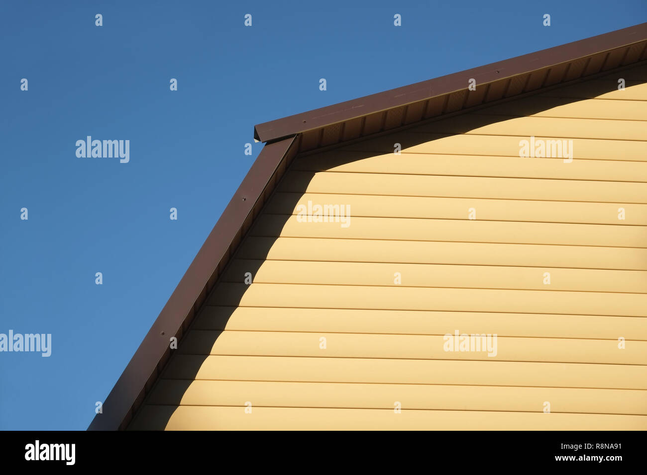 Parte della casa rurale parete ricoperta con schierandosi giallo e marrone e tetto metallico sul limpido azzurro cielo privo di nuvole sulla giornata soleggiata vista frontale closeup Foto Stock