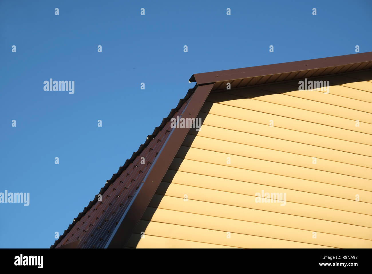 Parte della casa rurale parete ricoperta con schierandosi giallo e marrone e tetto metallico sul limpido azzurro cielo privo di nuvole sulla giornata soleggiata vista frontale closeup Foto Stock