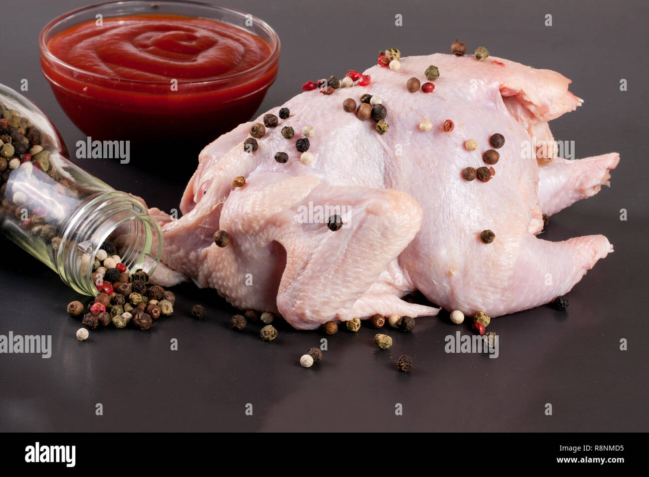 Il pollo crudo carcassa con chicchi di pepe nero su sfondo scuro Foto Stock