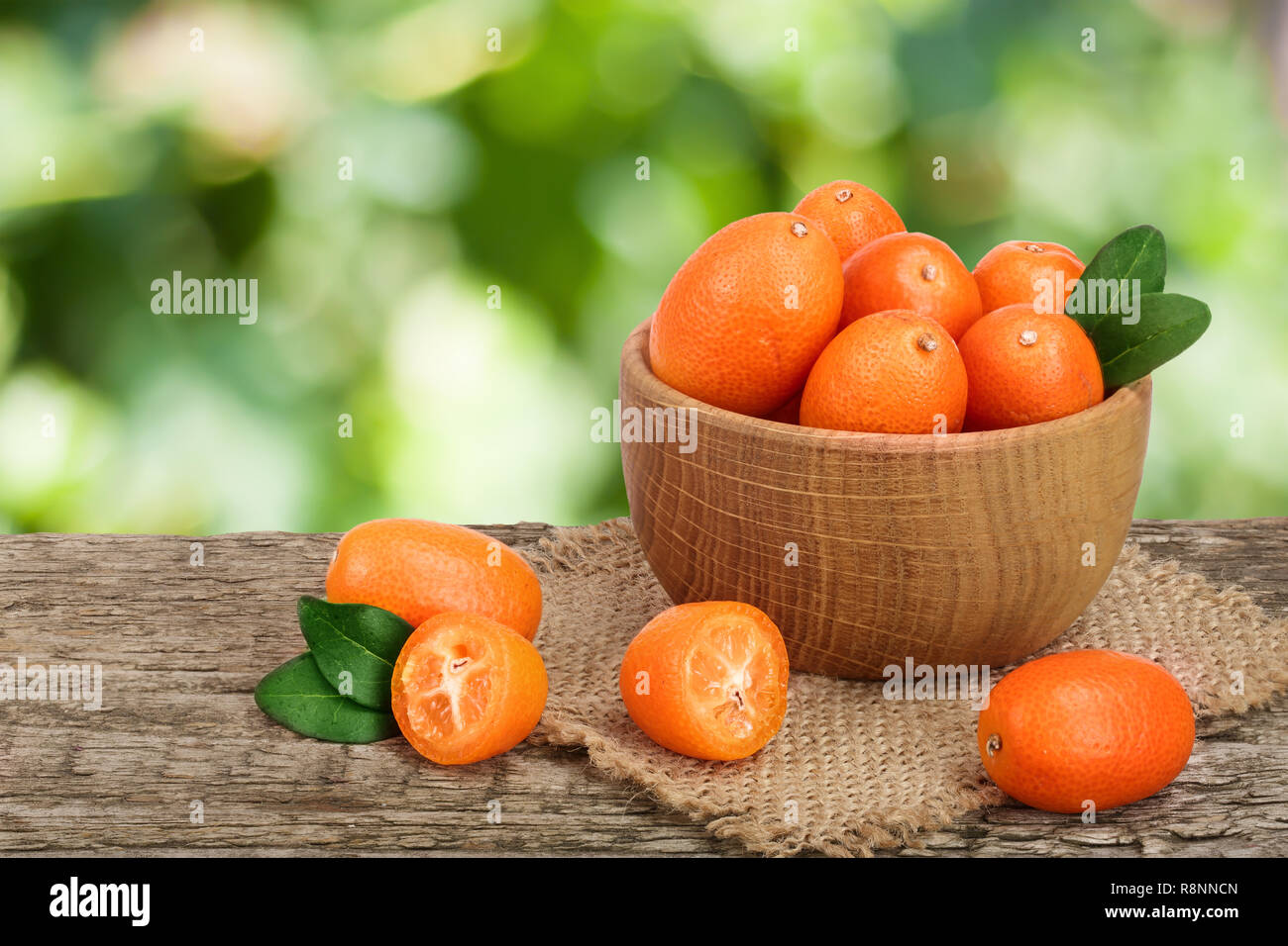 Cumquat o kumquat con foglia nella ciotola di legno sul vecchio tavolo in legno con giardino sfocate sullo sfondo Foto Stock