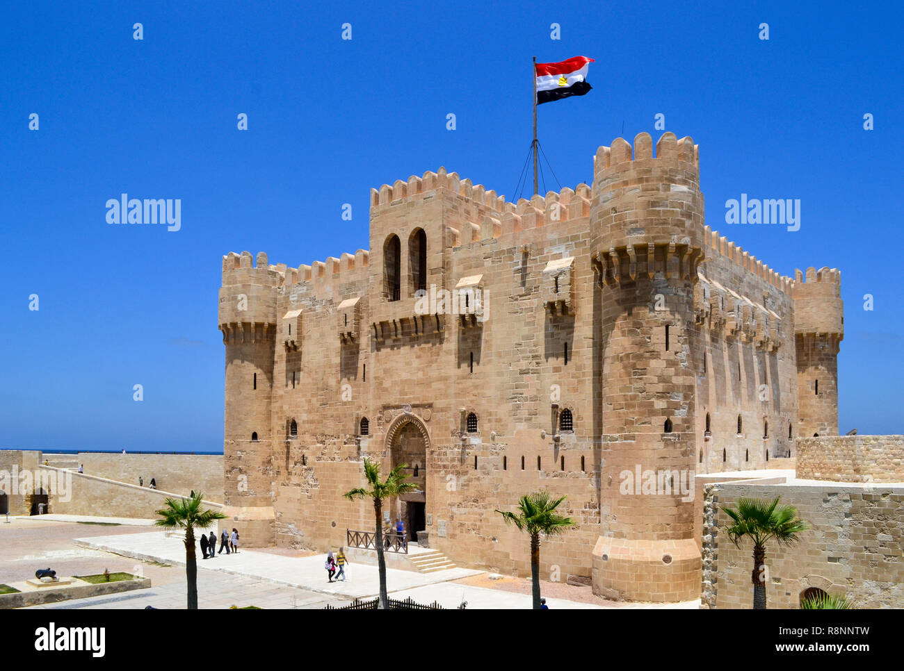 Nazionale Egiziano bandiera sventola su un ventoso giorno di sole sulla sommità della cittadella Qaitbay fortezza - castello come architettura. I turisti a piedi Foto Stock