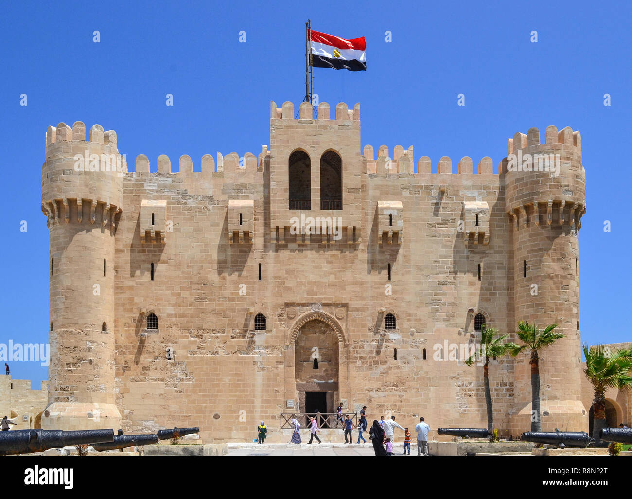 I turisti a piedi sui giardini della cittadella Qaitbay sotto un sole forte in Egitto. La città di Alessandria sito turistico. Foto Stock