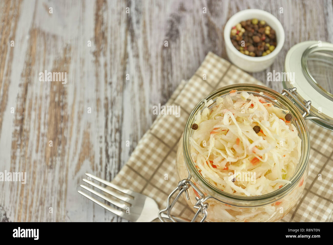 Un vasetto di crauti e carote nel proprio succo con spezie su una luce bianca, tavolo in legno, un verticale tipo di cavolo cappuccio in un vaso tradizionale home-m Foto Stock