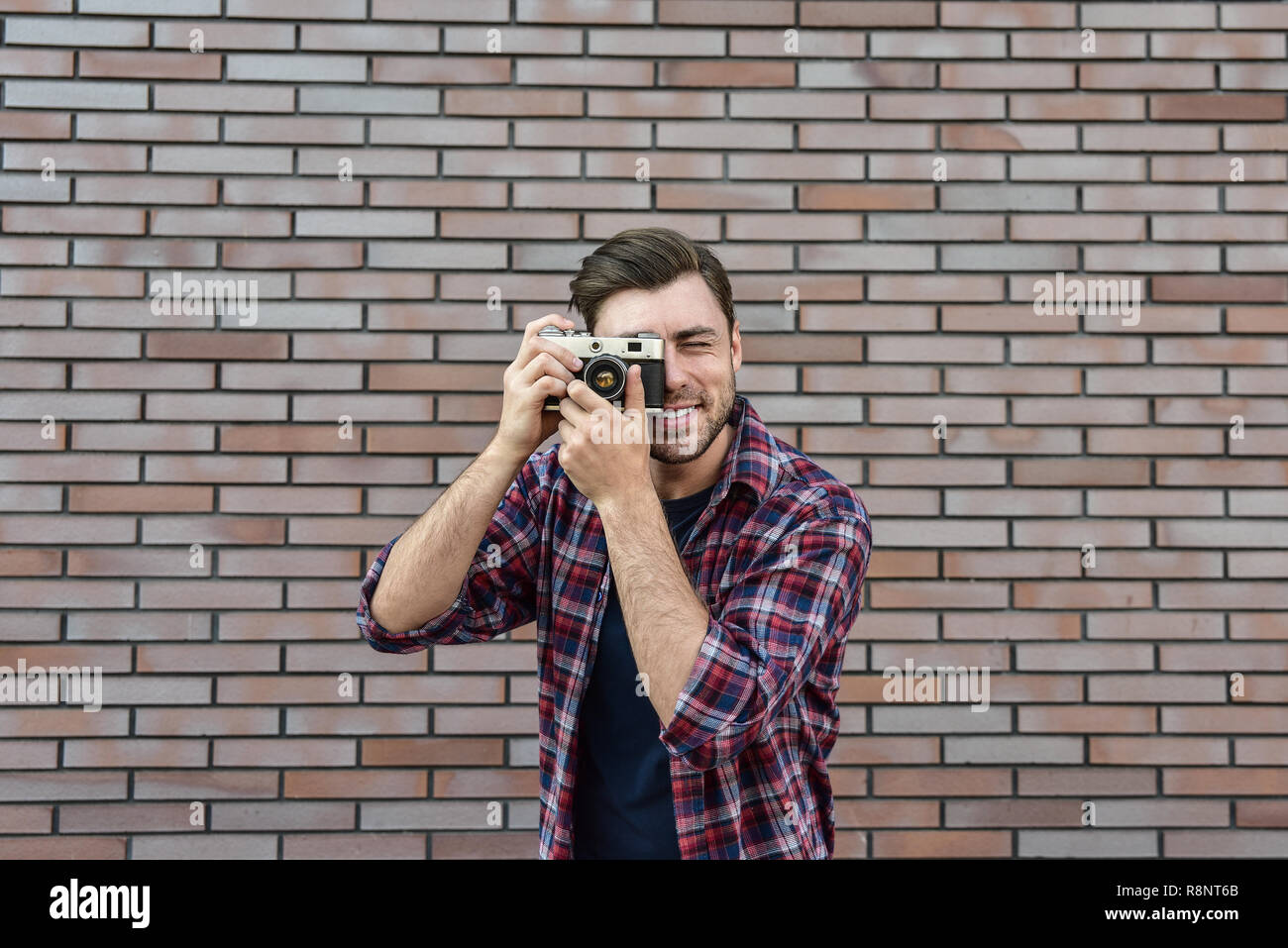 Uomo con retrò fotocamera foto di moda stile di vita viaggio outdoor mentre in piedi contro un muro di mattoni dello sfondo. Foto Stock