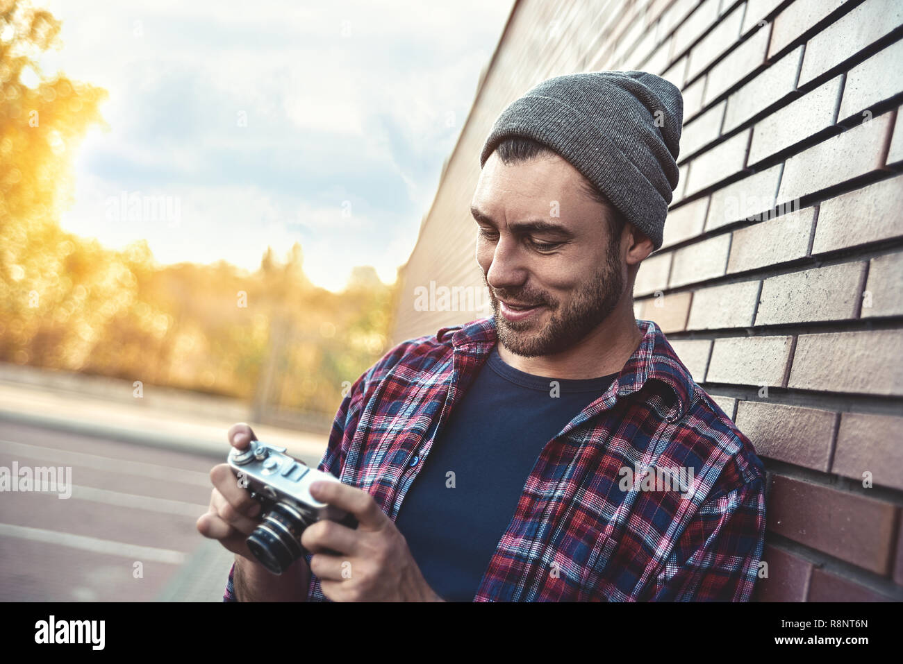 Uomo sorridente con retrò fotocamera foto di moda stile di vita viaggio outdoor mentre in piedi contro un muro di mattoni sfondo Foto Stock