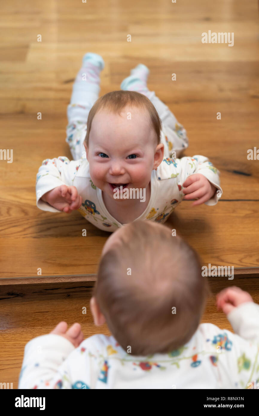 La riflessione di un nove mesi ragazza bambino guardando in uno specchio e sorridente al visualizzatore Foto Stock