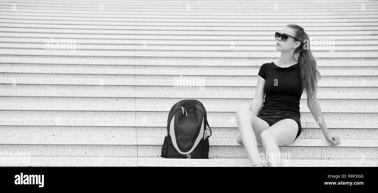 Ragazza rilassante turistica su terreni sassosi scale vicino al suo zaino. Prendere minuto per rilassarsi. Occhiali da sole donna elegante abito nero di Parigi a piedi. Vacanze e viaggi concetto. Basso costo tour esplorare l'Europa. Foto Stock