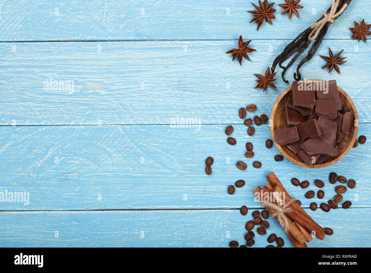 Cioccolato, bastoncini di vaniglia, cannella, i chicchi di caffè in blu sullo sfondo di legno con una copia dello spazio per il tuo testo. Vista superiore Foto Stock