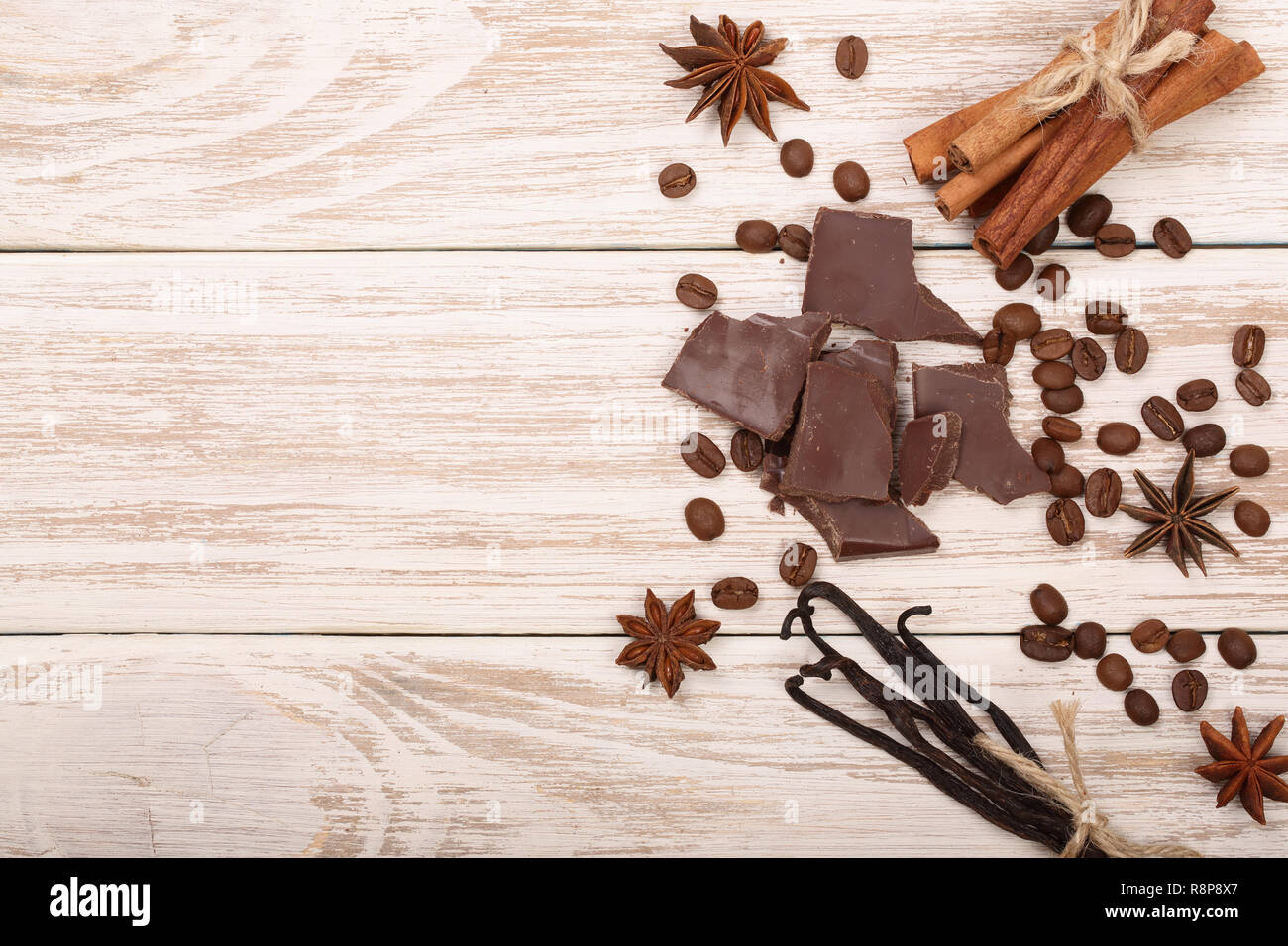 Cioccolato, bastoncini di vaniglia, cannella, i chicchi di caffè in bianco sullo sfondo di legno con una copia dello spazio per il tuo testo. Vista superiore Foto Stock