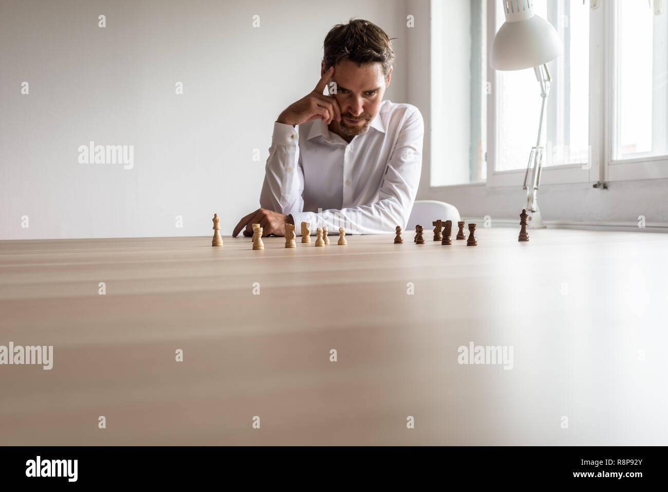 Young business leader executive ubicazione alla sua scrivania con squadre di bianco e nero a scacchi pezzi su hiss office desk fare decisioni hr. Foto Stock