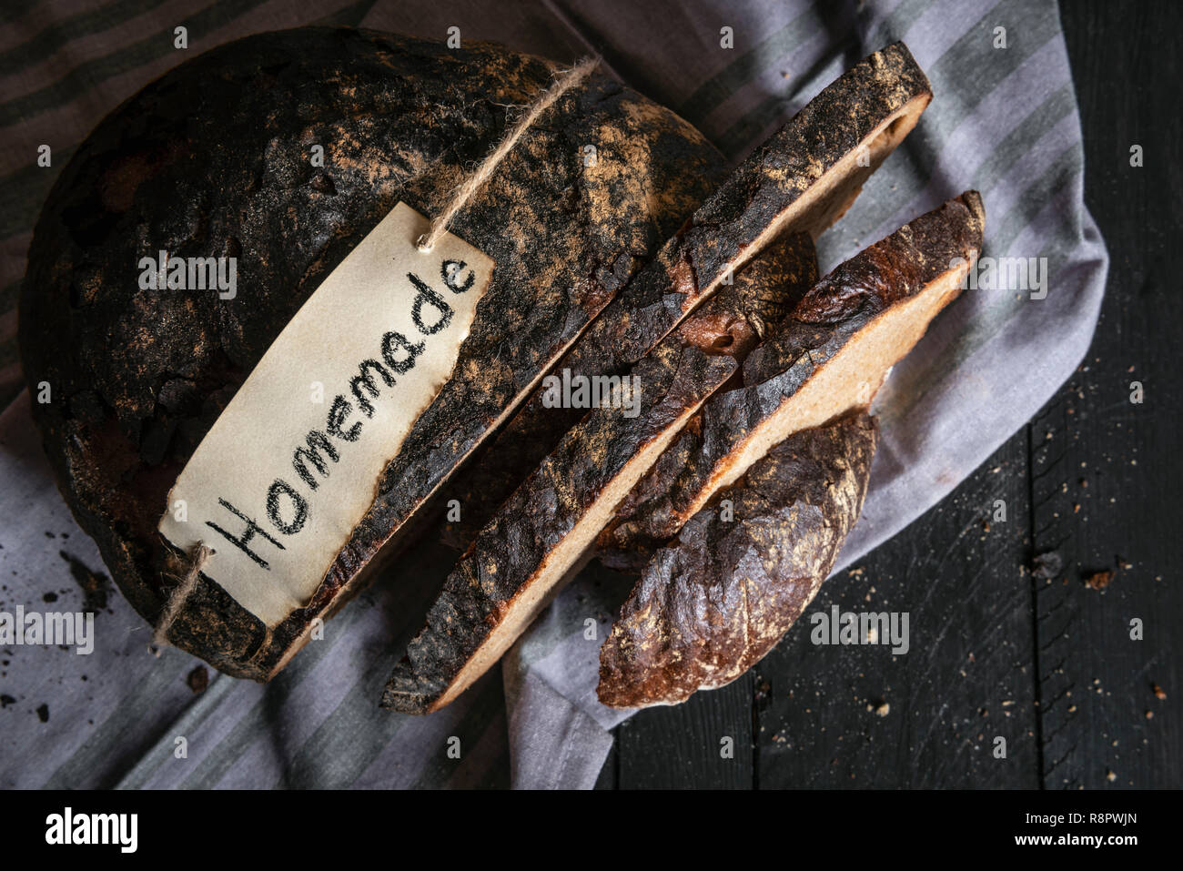 Fette di pane marrone con fatti in casa etiquette, su un asciugamano, su un rustico tavolo nero. Al di sopra di vista del tedesco tradizionale pane di segale. Pane appena sfornato. Foto Stock