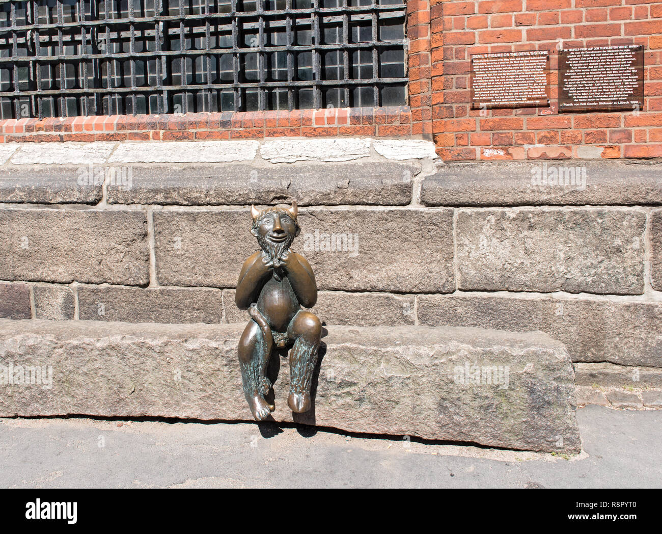 Metallo piccolo diavolo seduto su un gradino di pietra di fronte alla Marienkirche (St. Chiesa di Marys) a Lubecca, Germania Foto Stock