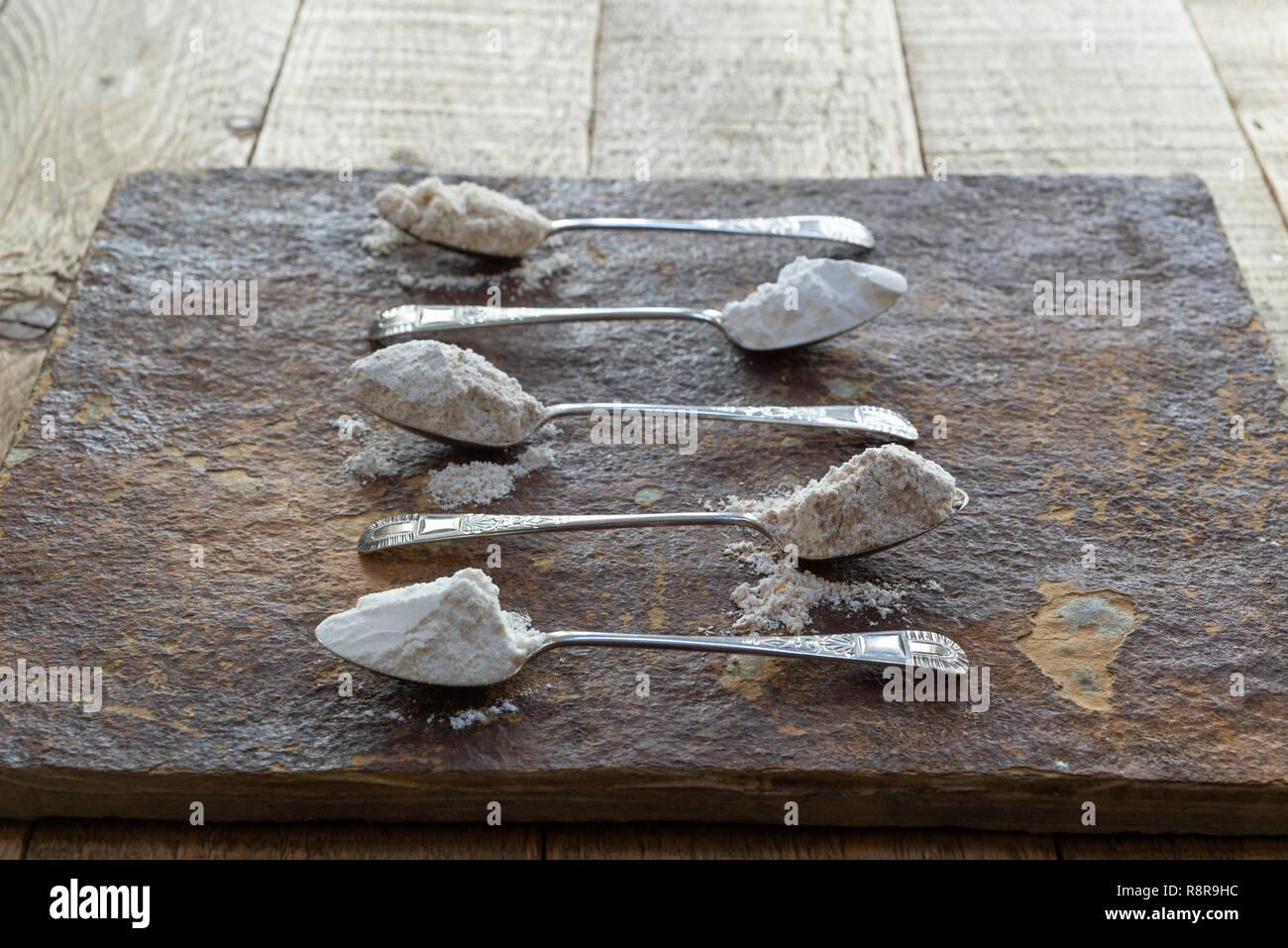 Cinque cucchiai di farine diverse. Dalla cima: farina di avena farina di riso, farina di segale, la farina integrale, la farina. Foto Stock