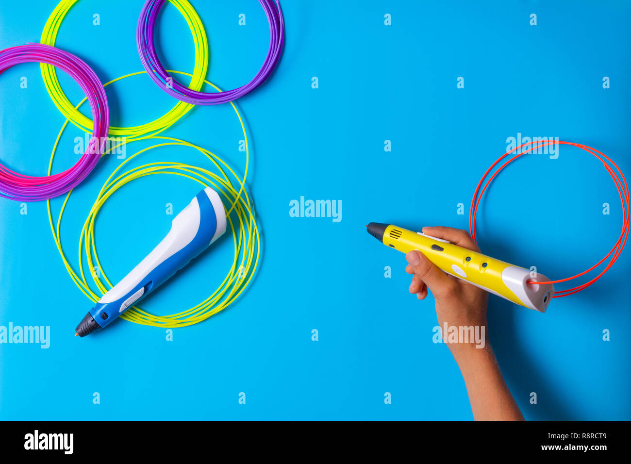 Kid mano azienda 3d penna con filamenti di plastica su sfondo blu Foto Stock