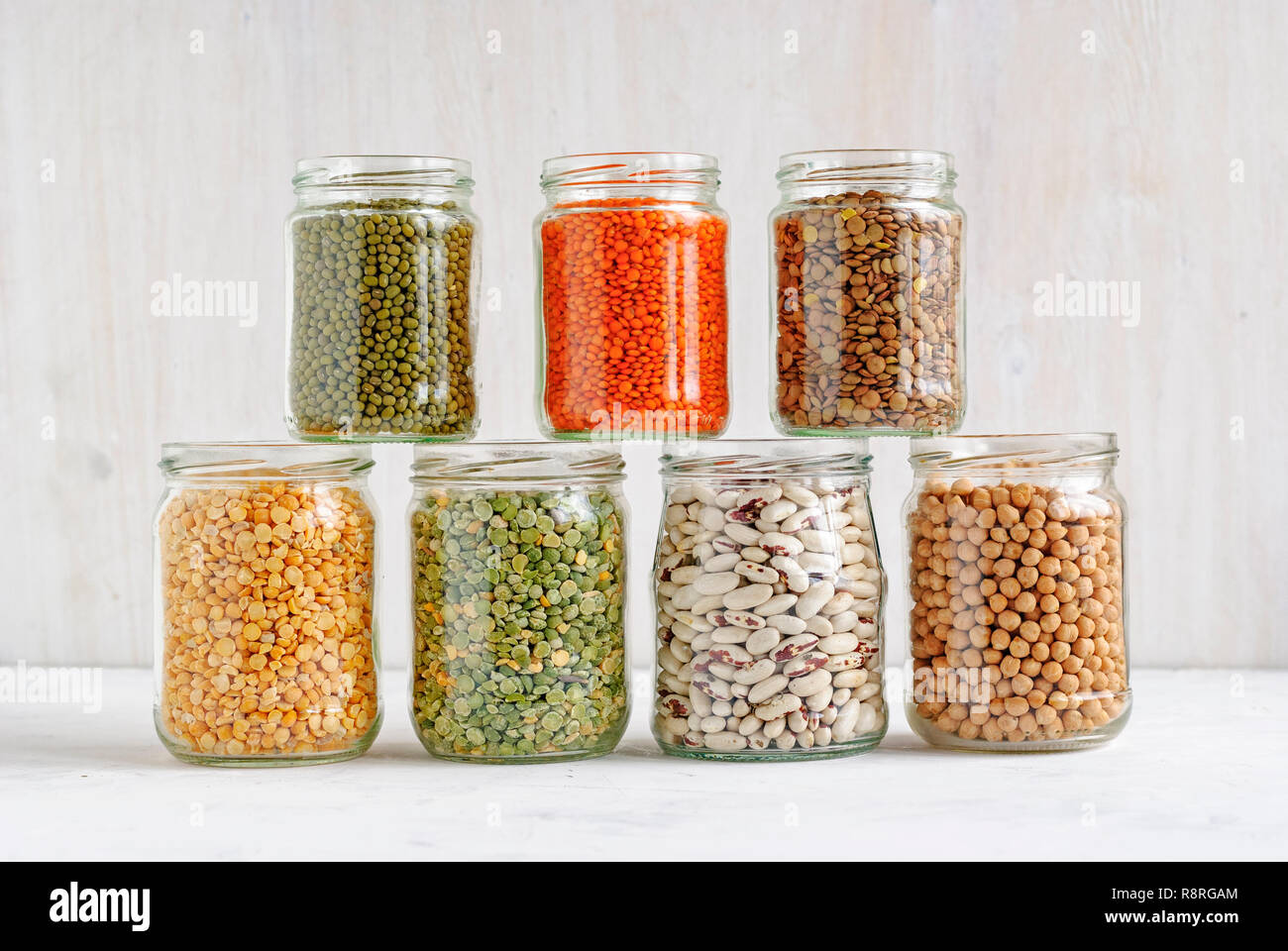 Fagioli, piselli, fagioli, lenticchie e ceci in vetro sovrapposti vasetti di storage su un muro bianco sullo sfondo ricco di proteine, di fibra alimentare e di vitamine Foto Stock