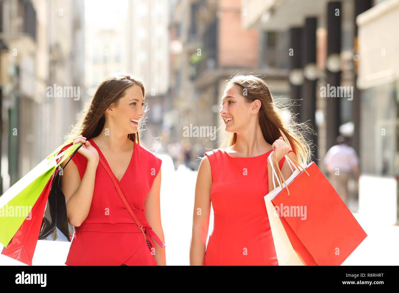 Vista frontale ritratto di due acquirenti felici parlando a piedi tenendo le borse della spesa in strada Foto Stock