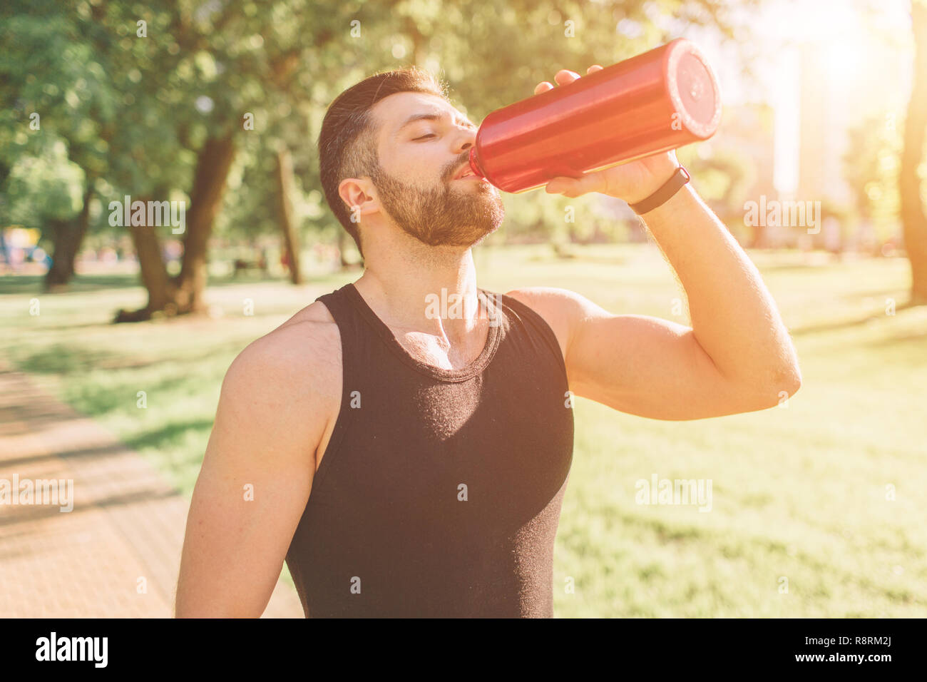Uomo con bottiglia di ferro e di acqua potabile. Giovane bello ben formati uomo sportivo riposo dopo la formazione all'esterno. Maschio modello fitness workout di formazione Foto Stock