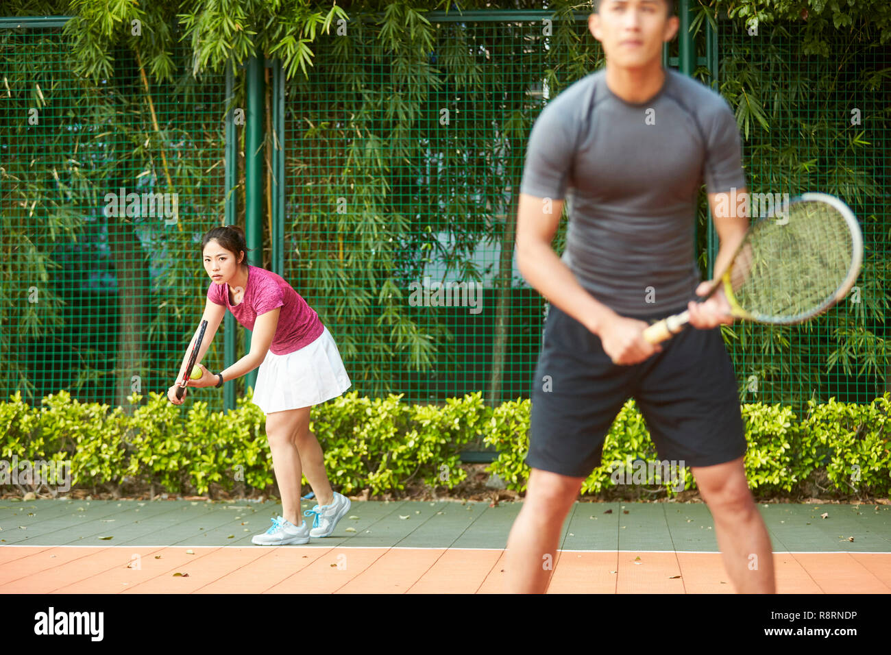Giovane donna asiatica di giocatore di tennis pronto a servire in un misto di partita doppia Foto Stock