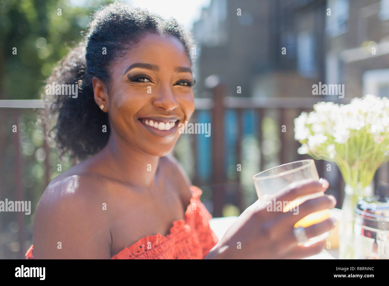 Ritratto sorridente, fiducioso giovane donna di bere succo di arancia sul balcone soleggiato Foto Stock
