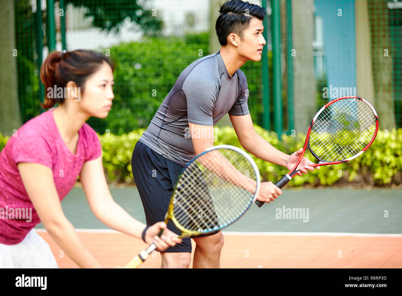 Giovane coppia asiatica di un uomo e di una donna i giocatori di tennis in un doppio misto corrispondono, concentrarsi sullo sfondo l'uomo Foto Stock