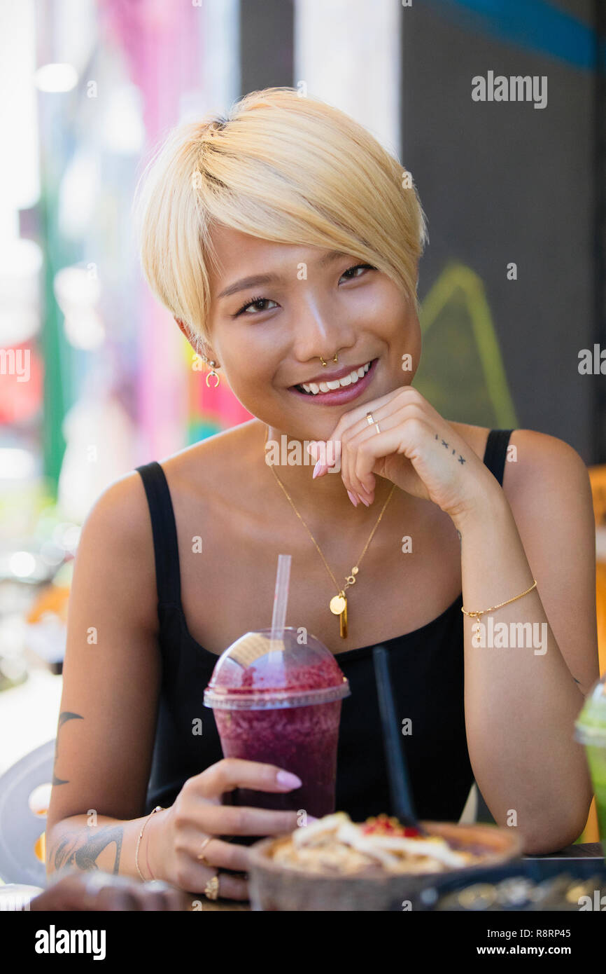 Ritratto sorridente, fiducioso giovane donna frullato da bere al cafè sul marciapiede Foto Stock