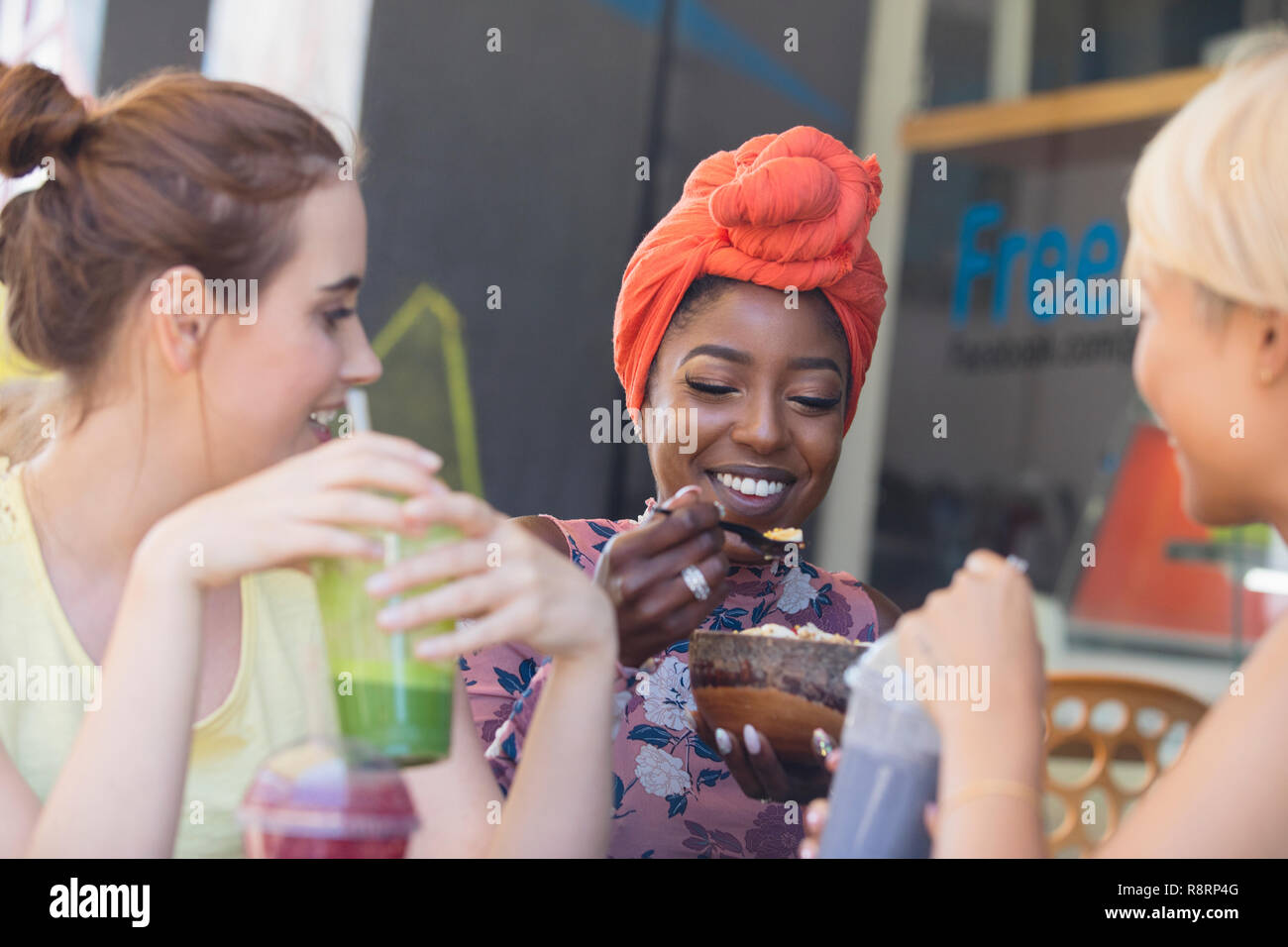 Giovani donne amici frullati a bere e mangiare al cafè sul marciapiede Foto Stock