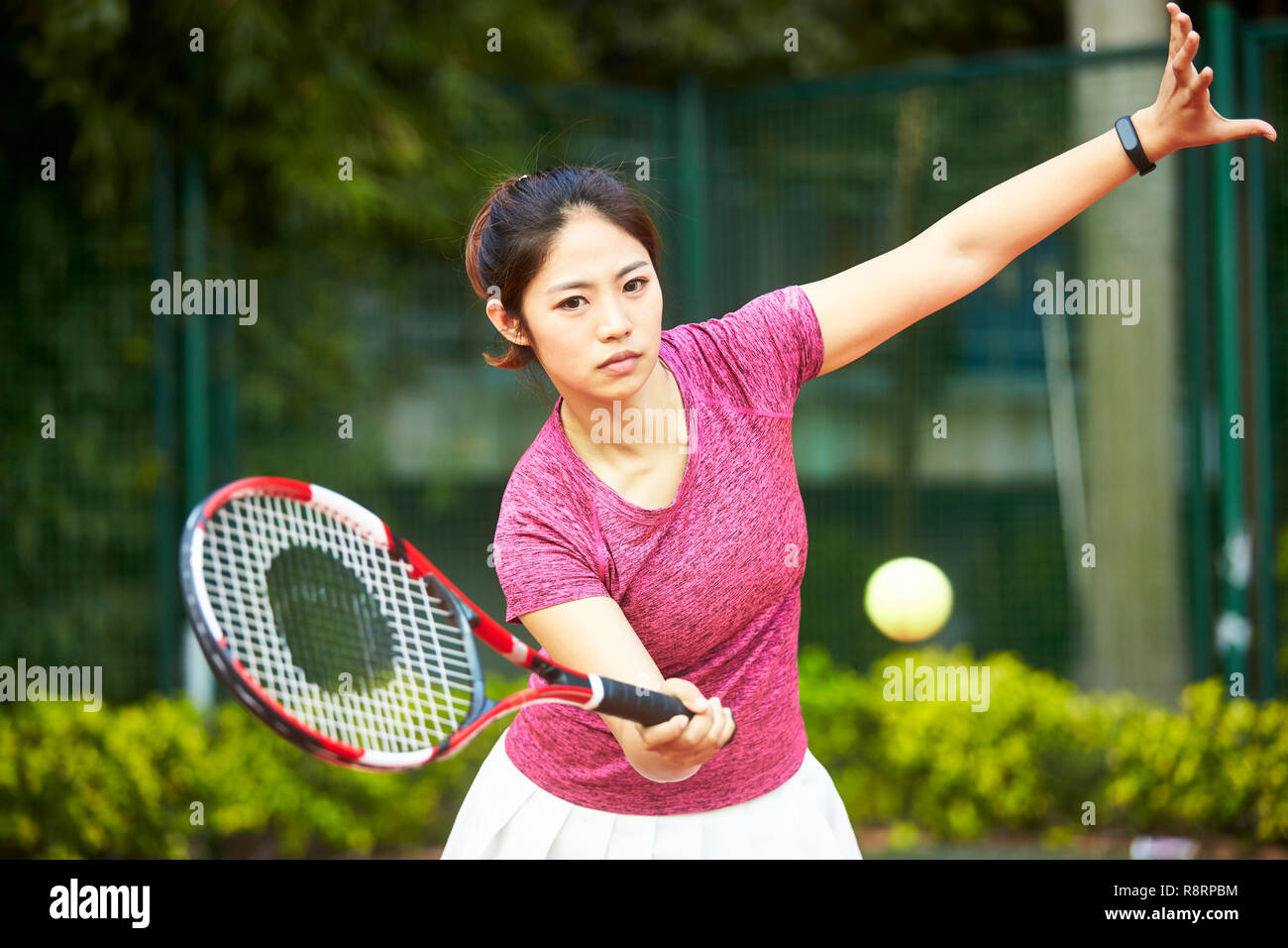 Giovane donna asiatica giocando a tennis all'aperto Foto Stock