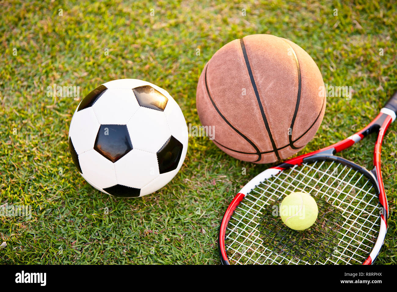 Il calcio pallone da calcio Basket Tennis palla e racket prevista sull'erba al tramonto, primo piano Foto Stock