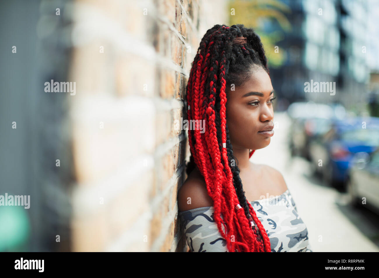 Fiducioso giovane donna con trecce rosso alla ricerca di distanza su strada urbana Foto Stock
