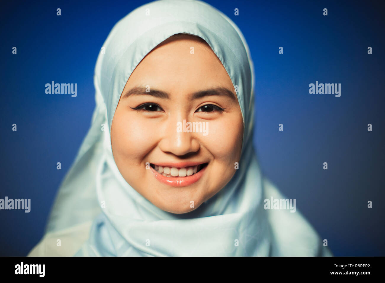 Close up ritratto sorridente, fiducioso giovane donna indossa seta blu hijab Foto Stock