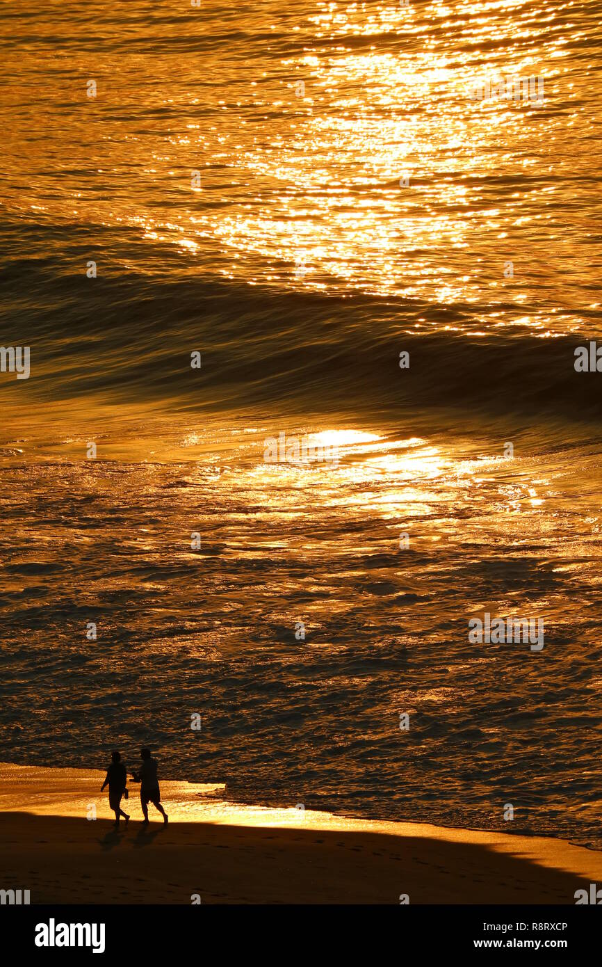 Oceano atlantico in golden luce del sole di mattina riflessioni con silhouette di due persone che camminano sulla spiaggia di Copacabana, Rio de Janeiro, Brasile Foto Stock