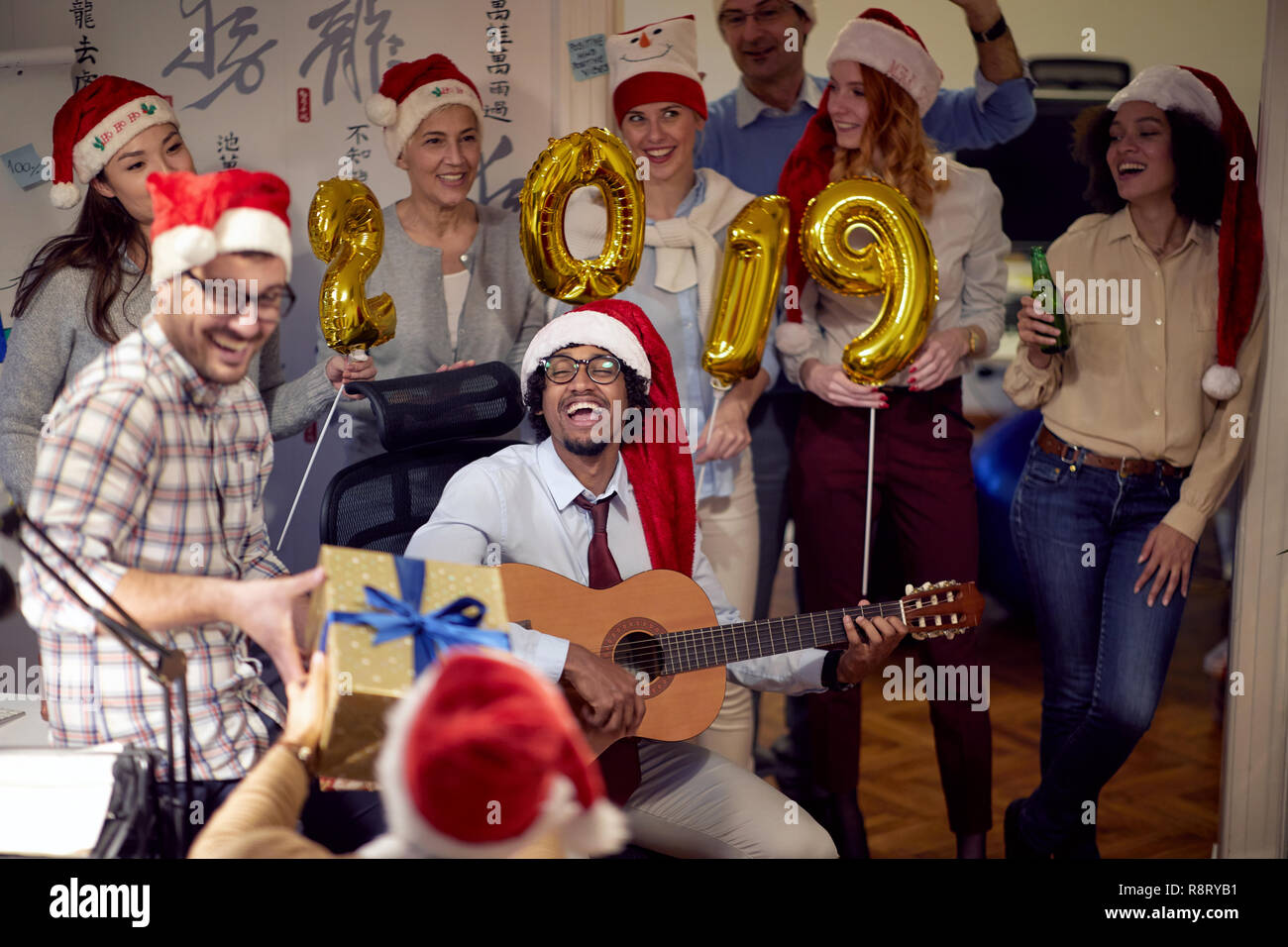 Felice di colleghi in Santa tappi aventi divertimento natalizio e suonare la chitarra in ufficio. Foto Stock