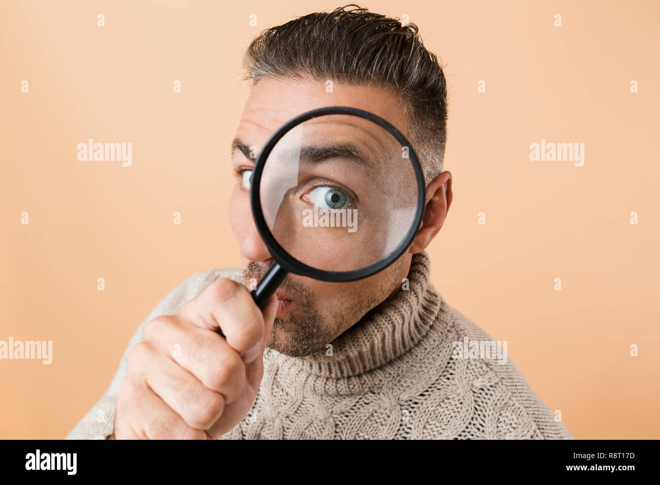 Close up a funny man guardando attraverso una lente di ingrandimento isolate su sfondo beige Foto Stock